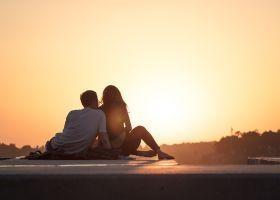 Ein Paar sitzt entspannt auf einer Mauer und genießt den Sonnenuntergang, die Nähe, die Zuwendung, die Wärme und Liebe. Eine gute Möglichkeit, sich gegenseitig die Wünsche und Bedürfnisse in der Partnerschaft mitzuteilen